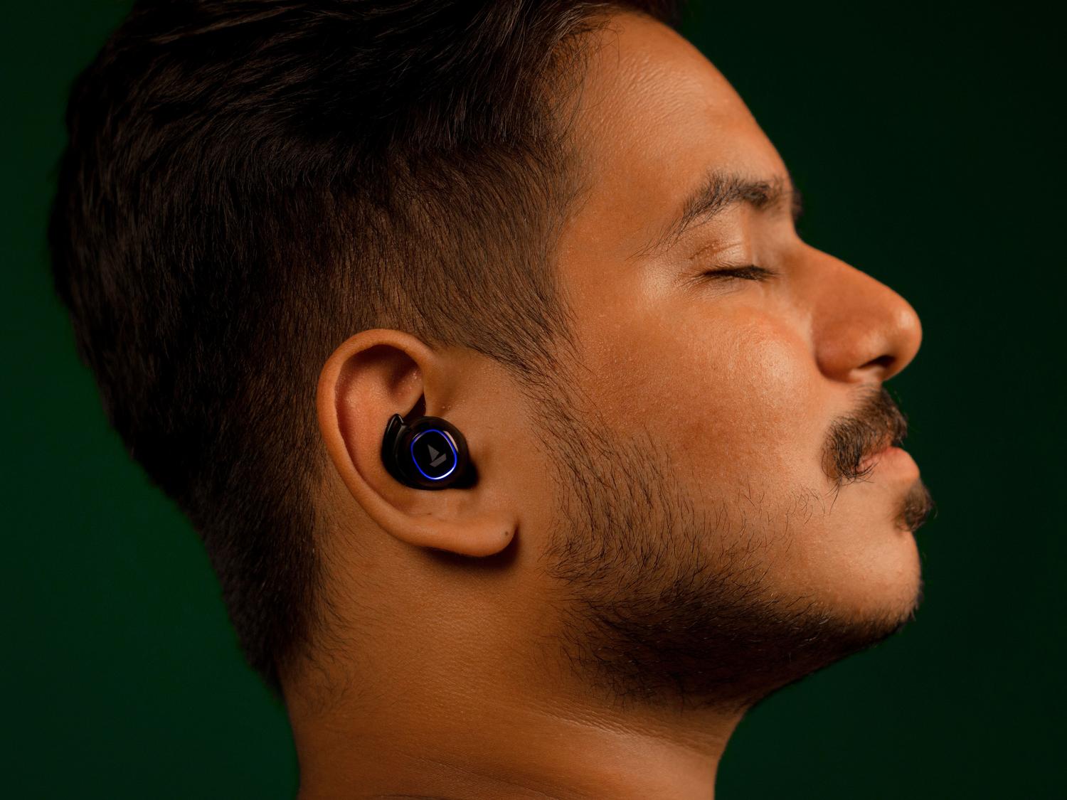 Primer plano de un hombre disfrutando de la música con auriculares TWS, con los ojos cerrados, transmitiendo una experiencia de sonido inmersiva.
