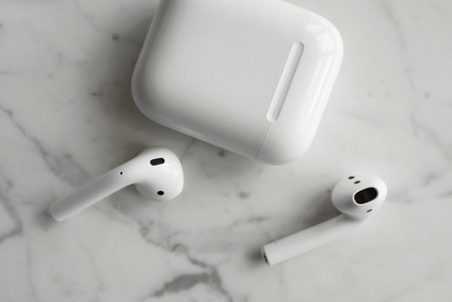 Auriculares TWS y estuche de carga sobre una superficie de mármol blanca, representando la tecnología moderna y minimalista.