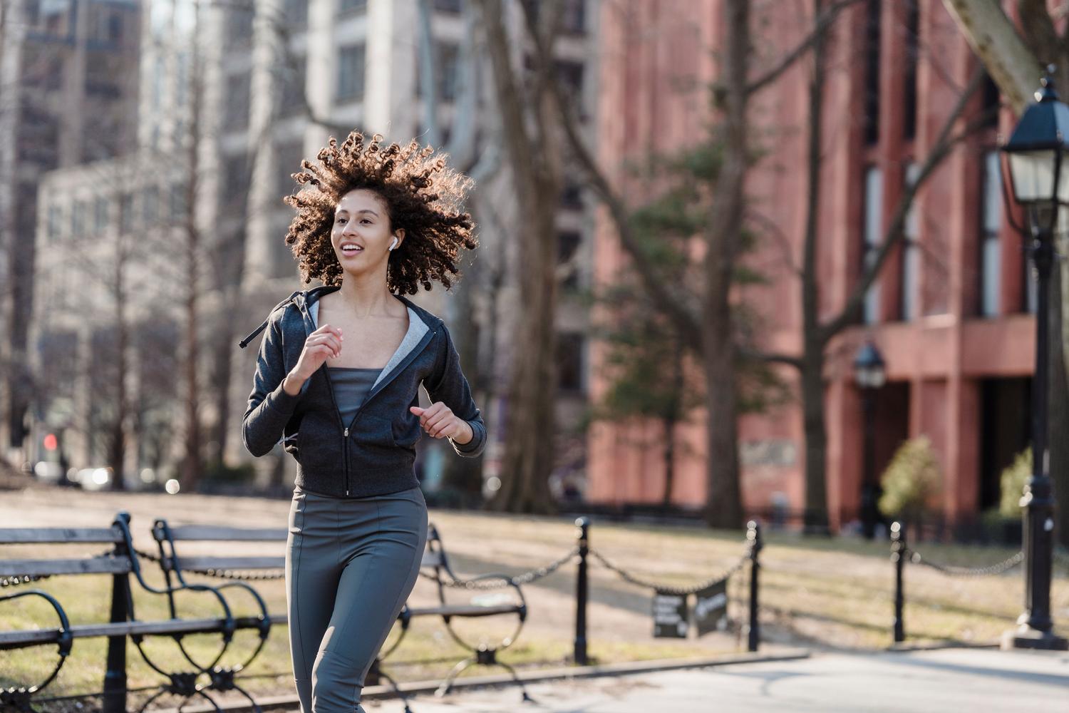 Mujer corriendo por la ciudad utilizando auriculares TWS, demostrando el ajuste seguro y la comodidad durante la actividad deportiva.