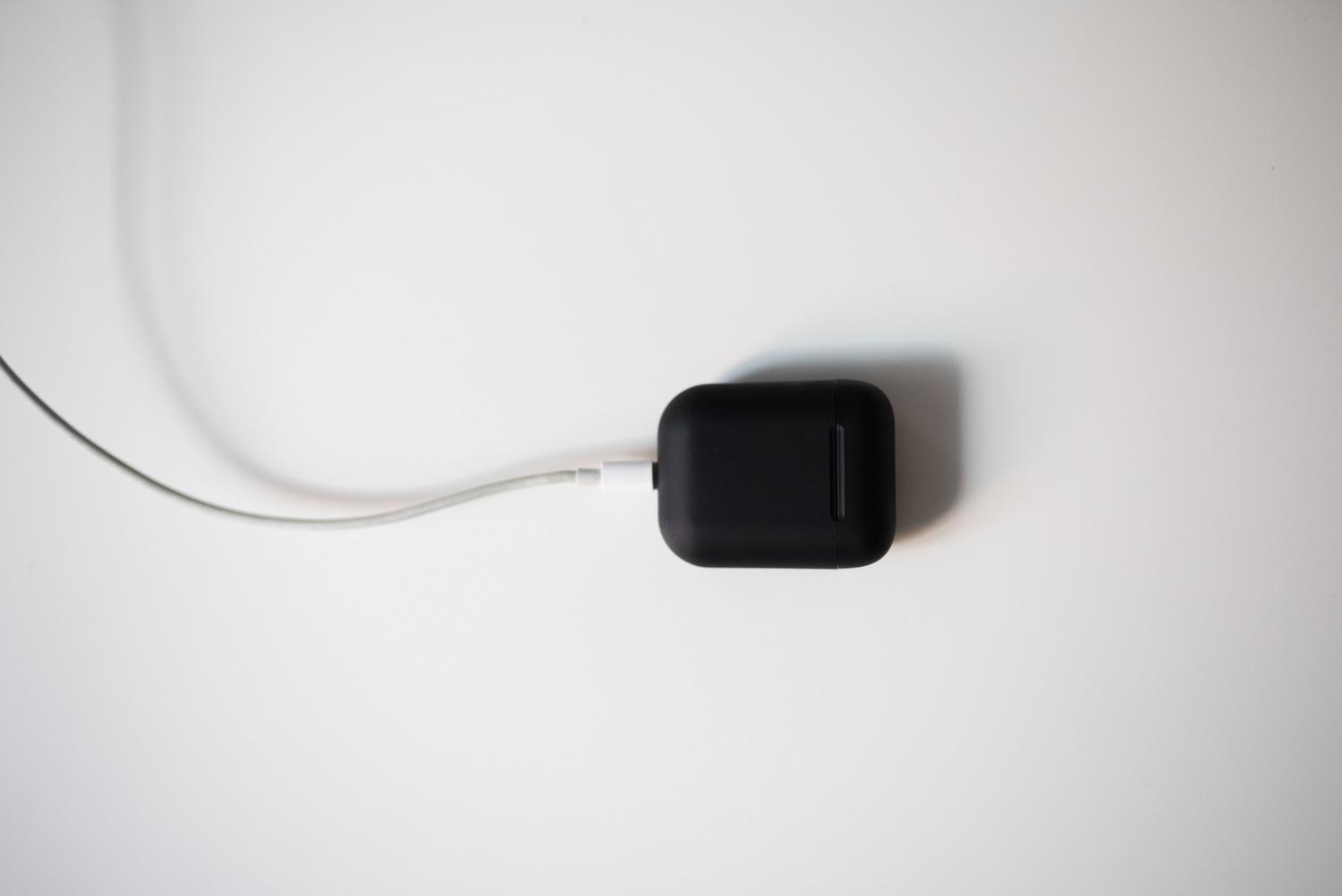 Estuche de carga de auriculares TWS conectado a un cable de carga sobre un fondo blanco, representando la autonomía y la recarga de energía.