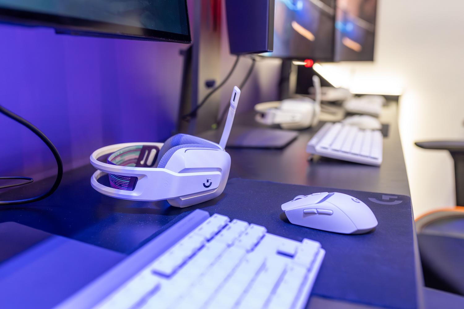 Primer plano de auriculares y ratón gaming sobre un escritorio con luces ambientales, destacando la integración entre hardware de alta calidad y software.