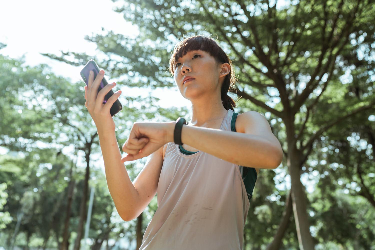 Mujer deportista en un parque sincronizando su smartwatch con la aplicación de salud en su teléfono móvil.