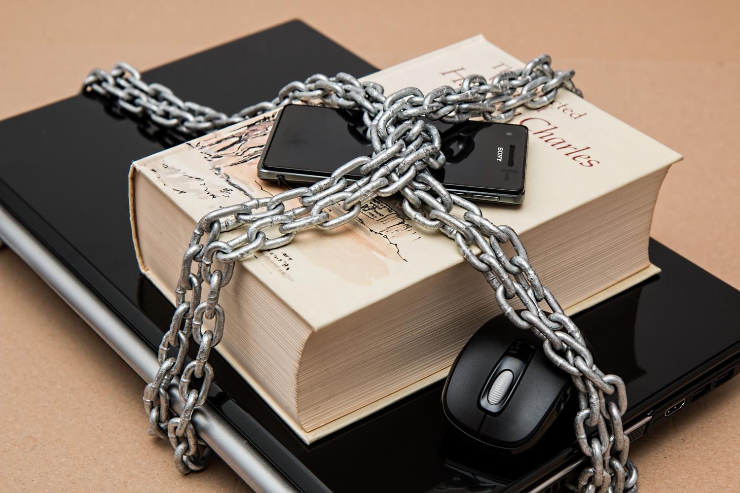 Smartphone y portátil encadenados, metáfora visual del ransomware y el secuestro de datos cifrados.