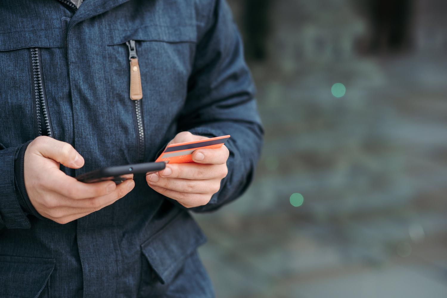 Persona introduciendo datos de tarjeta de crédito en un smartphone en la calle, ilustrando la vulnerabilidad de las transacciones en entornos públicos.