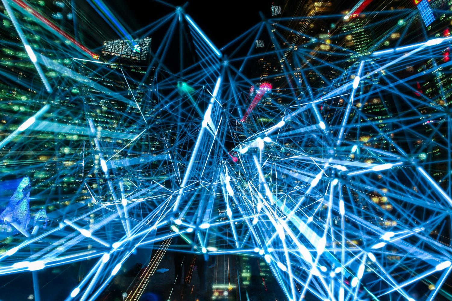 Ciudad futurista con trazos de luz azul que ilustran la red de comunicación digital y el flujo de datos de la infraestructura de IA.
