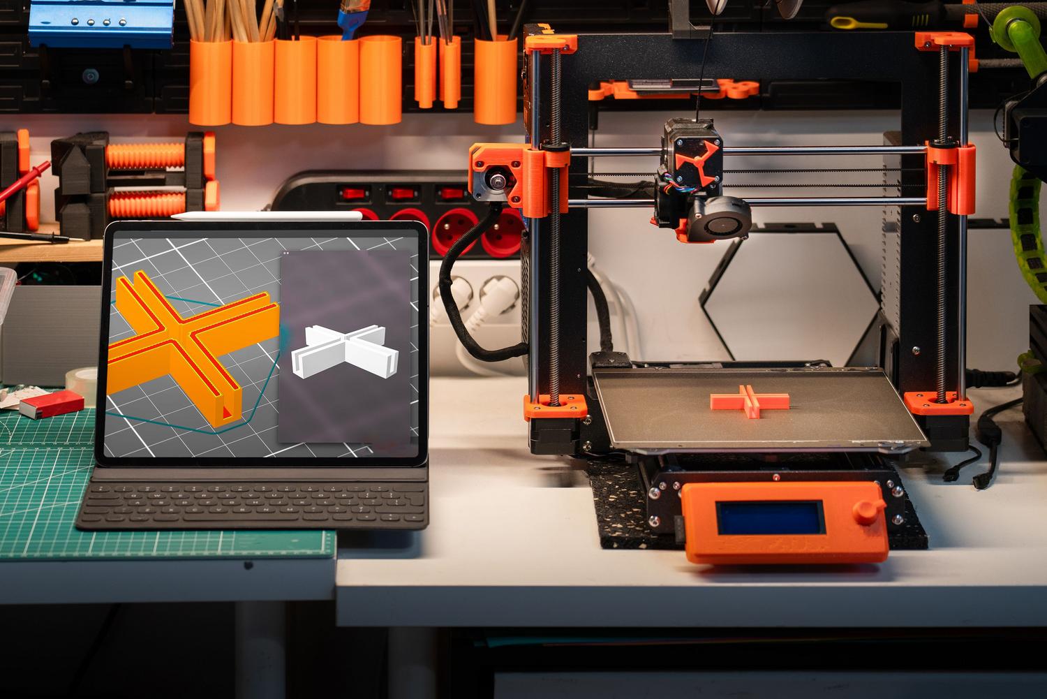 Espacio de trabajo profesional con una impresora 3D y un ordenador mostrando modelos tridimensionales.