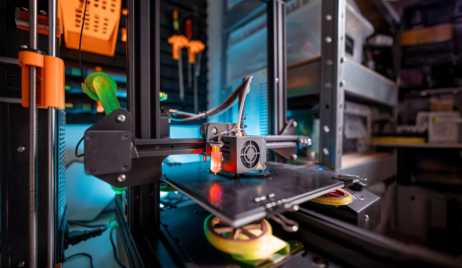 Primer plano de una impresora 3D trabajando en un entorno de taller, destacando la tecnología de fabricación aditiva.