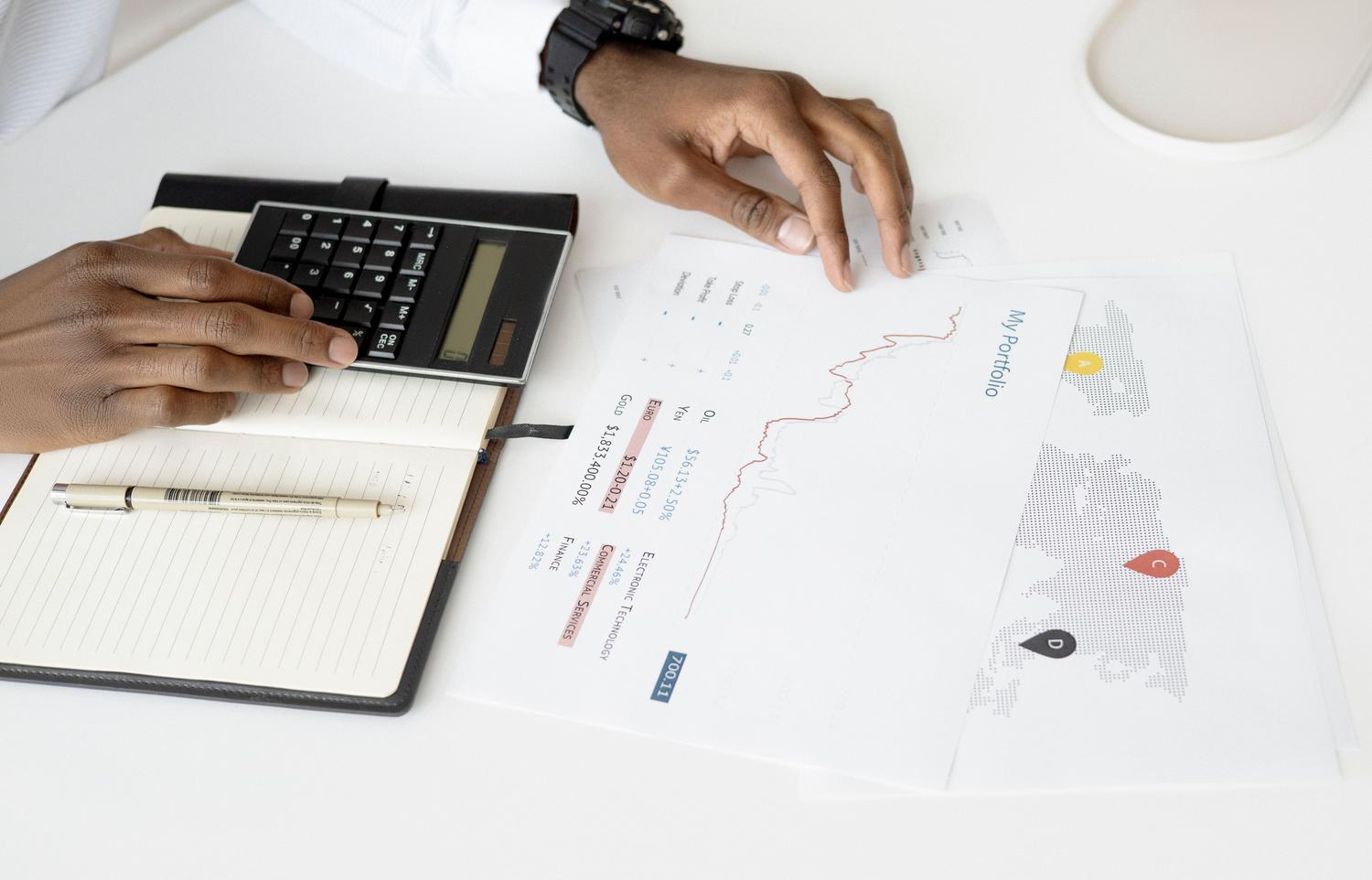 Close-up of a professional analyzing financial portfolio data on a desk, using a calculator and reviewing charts and maps.