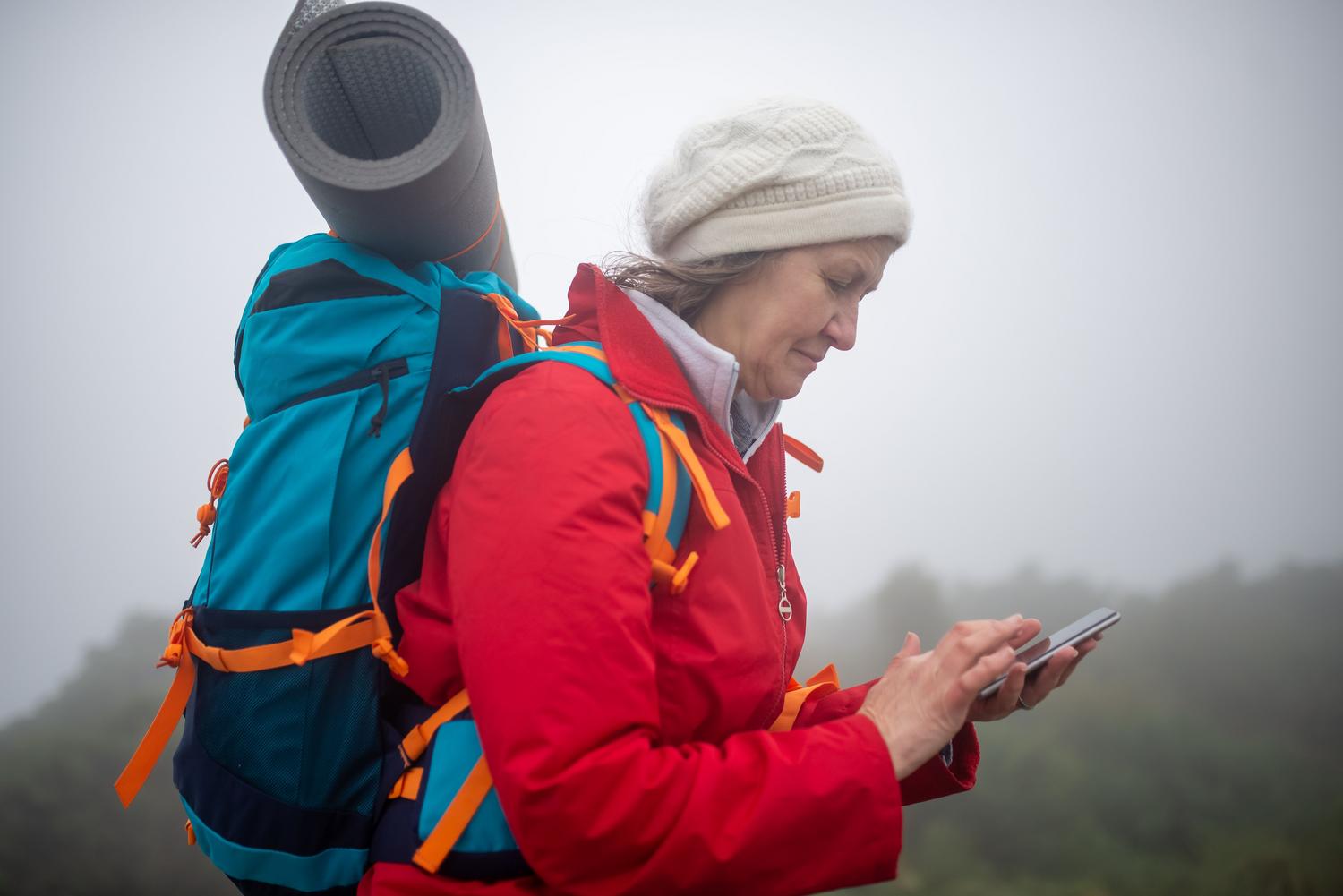 Senderista comprobando su smartphone en medio de una densa niebla, resaltando la importancia de la red satelital en situaciones de emergencia o rutas aisladas.