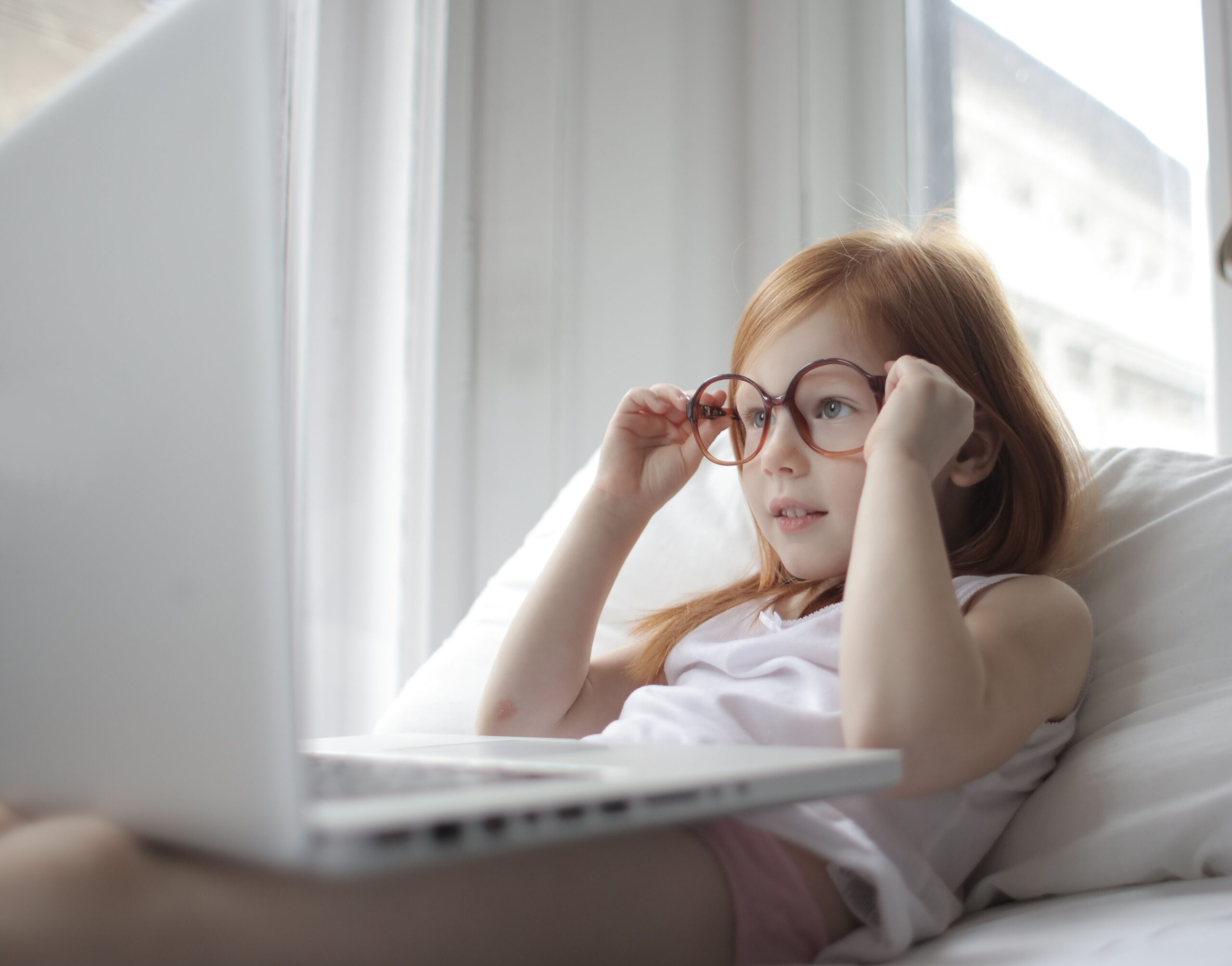 Niña con gafas utilizando un ordenador portátil, ilustrando el impacto de las pantallas en la visión infantil