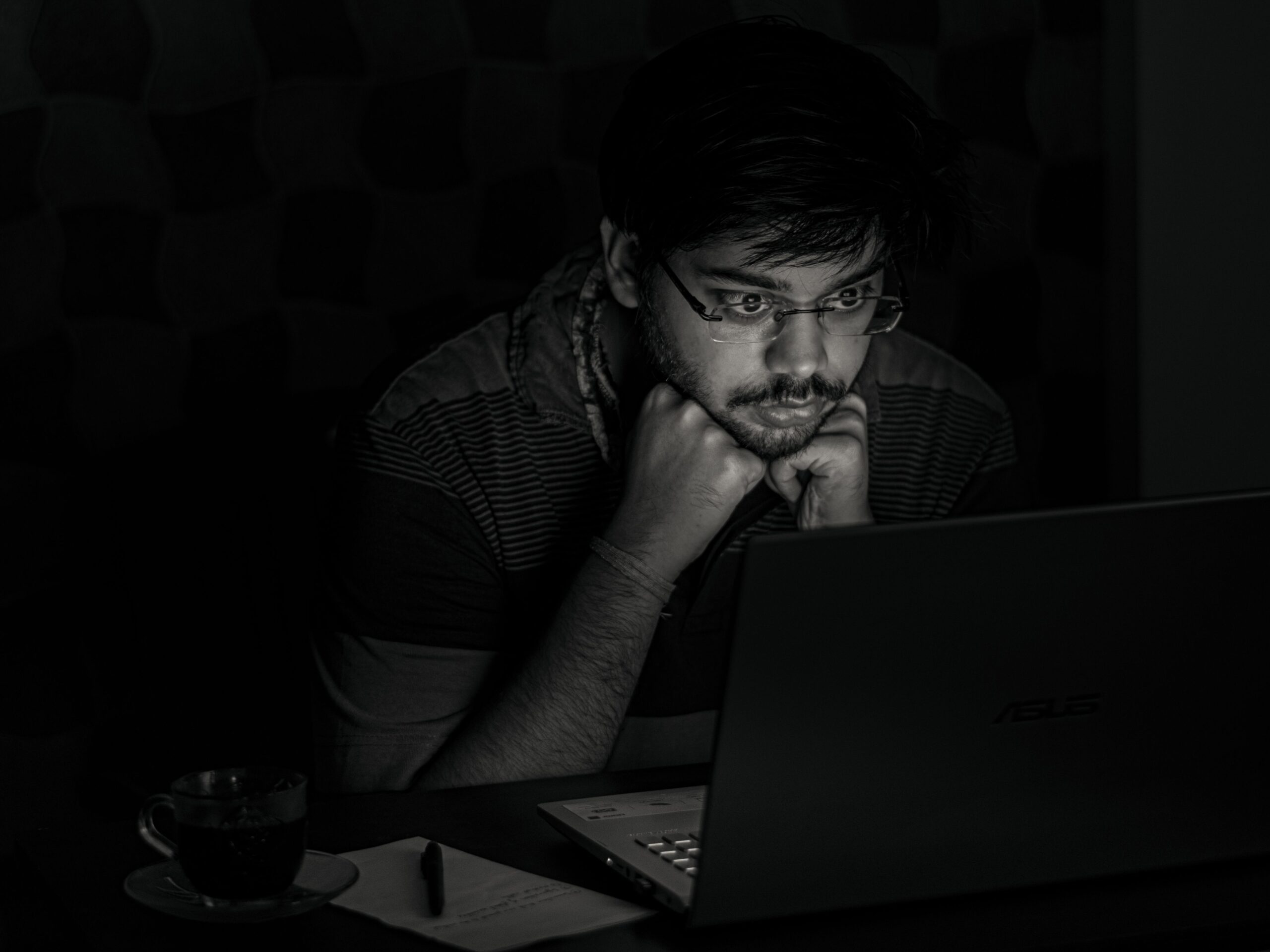Hombre trabajando en una habitación oscura con la luz del monitor, ejemplo de iluminación deficiente que causa fatiga visual