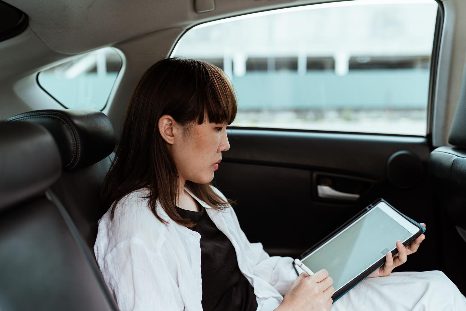 Mujer utilizando una tablet con lápiz óptico en el asiento trasero de un coche, representando la movilidad y conectividad 5G.