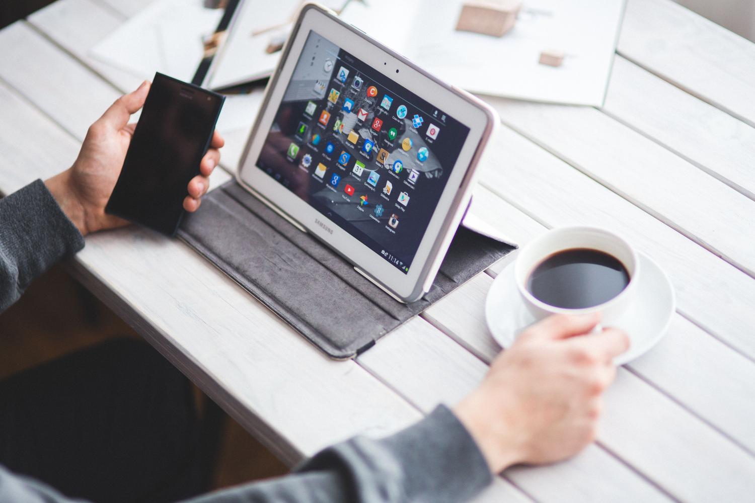 Persona trabajando con una tablet y un café en una mesa de madera, ilustrando el teletrabajo y la versatilidad del dispositivo.