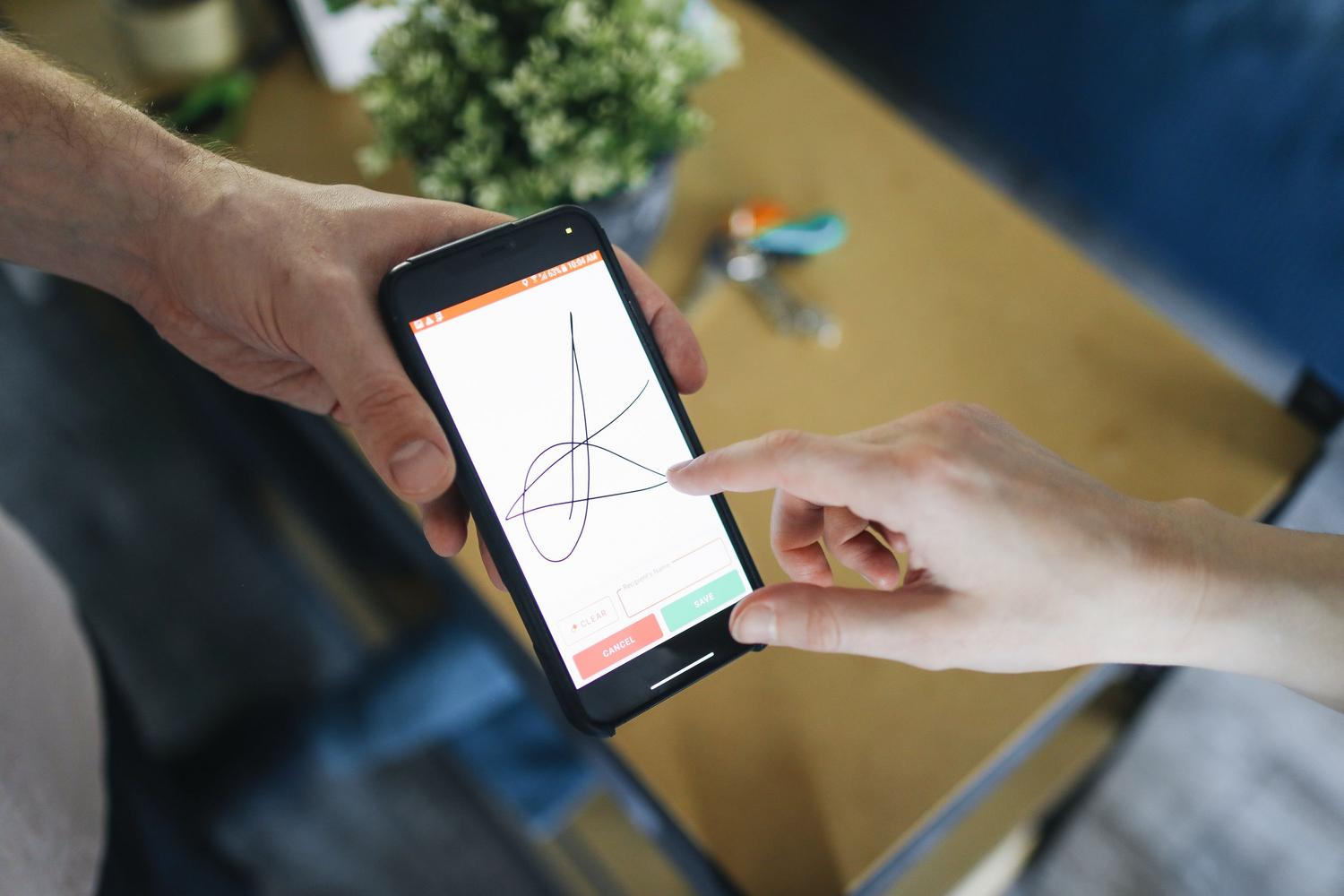 Dos personas realizando una firma digital en la pantalla de un smartphone, ilustrando el proceso de firma electrónica y movilidad.