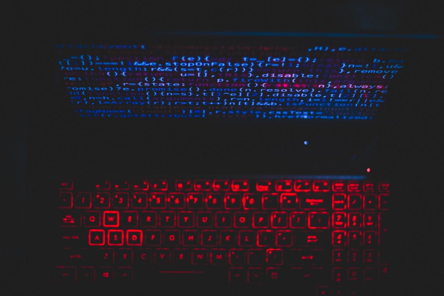 Primer plano de un portátil con código de programación en pantalla y teclado retroiluminado en rojo, evocando una interfaz de línea de comandos.