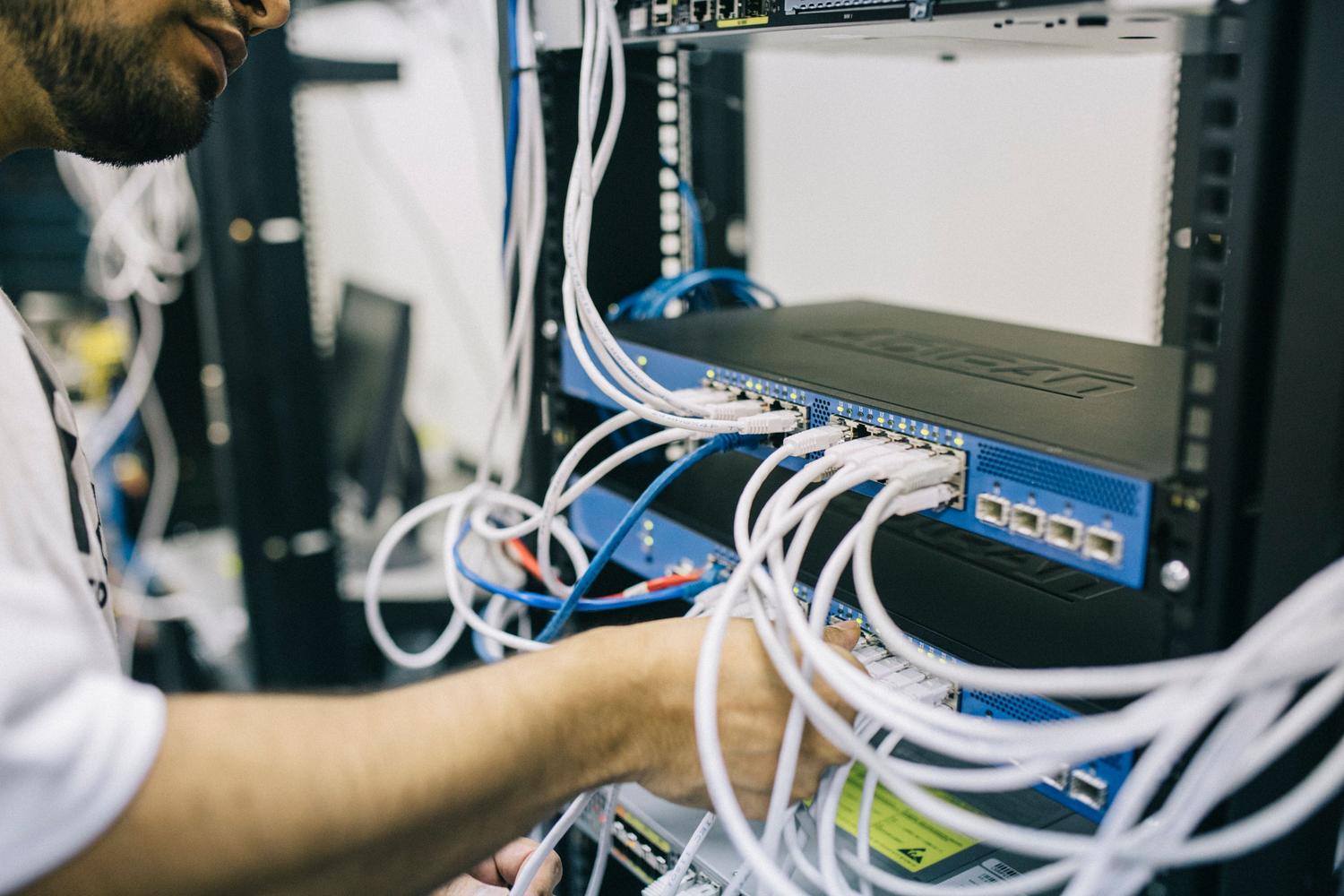 Técnico de IT gestionando el cableado de red en un rack de servidores profesionales.