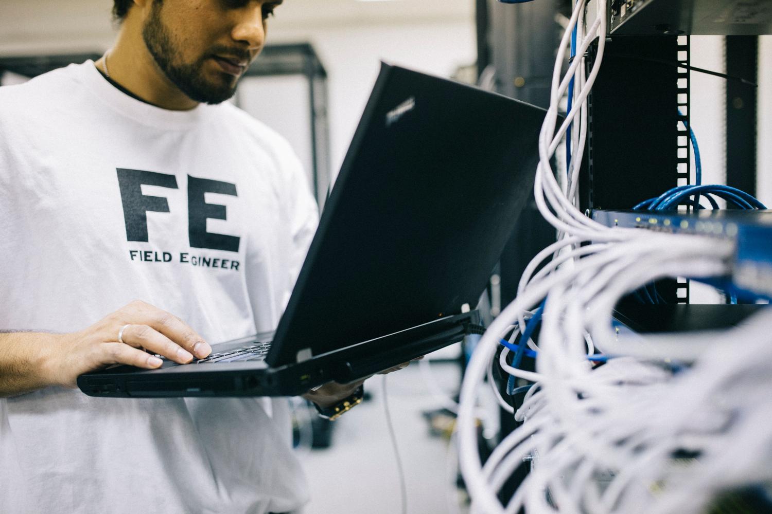 Ingeniero de campo utilizando un portátil para diagnosticar y configurar hardware en un rack de servidores.