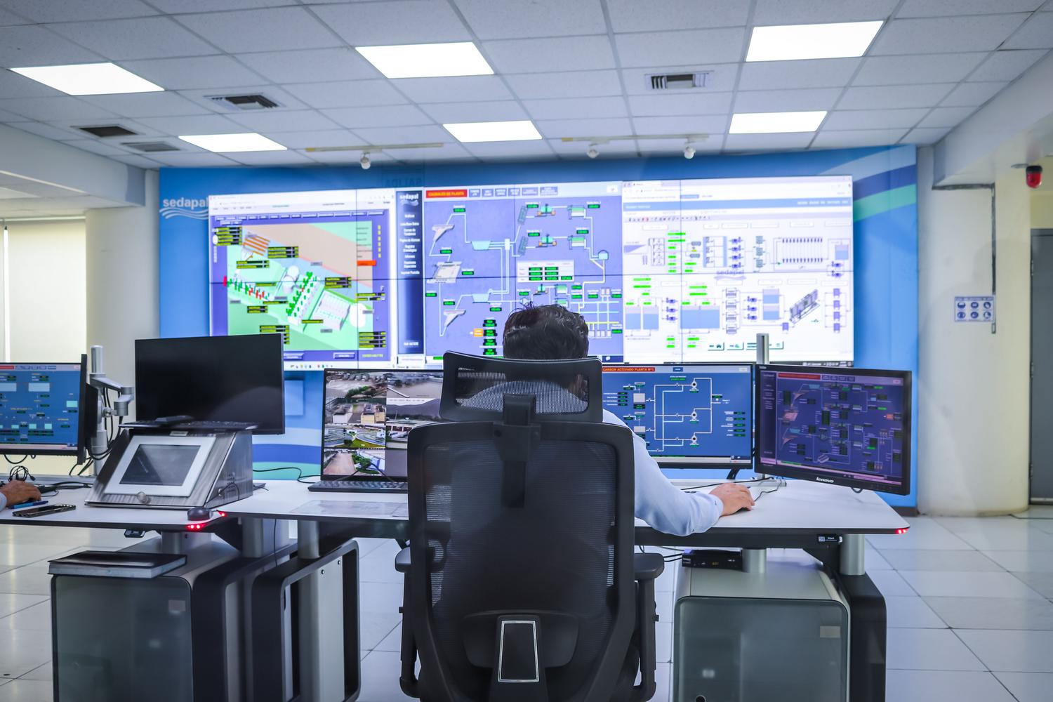 Operador gestionando sistemas tecnológicos en una sala de control industrial moderna