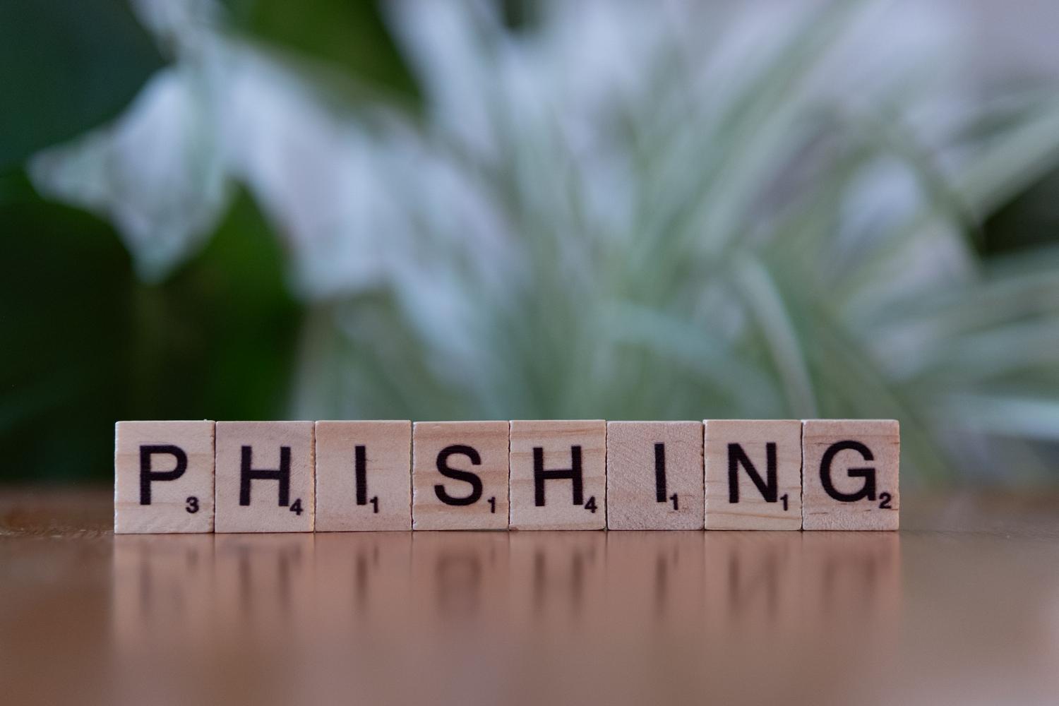 Fichas de madera tipo Scrabble deletreando la palabra 'Phishing', ilustrando el concepto de engaño y ciberataques.