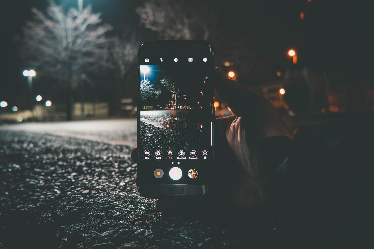 Primer plano de un smartphone ajustando el ISO y la velocidad de obturación para una foto nocturna urbana.