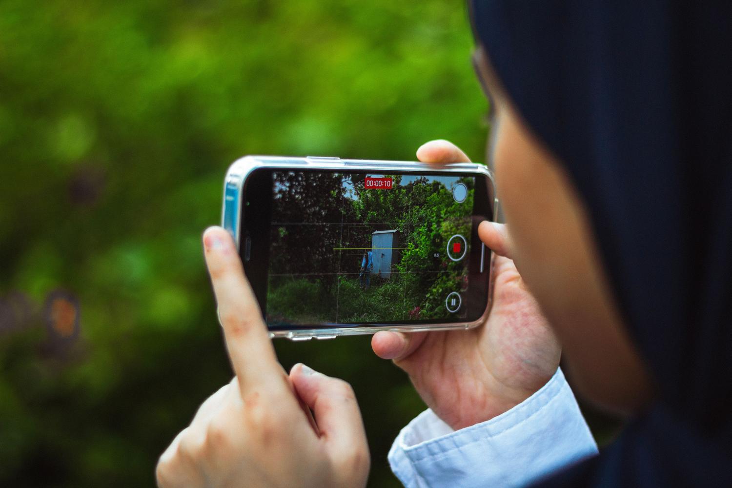 Primer plano de una persona grabando un paisaje verde con su smartphone, destacando la interfaz de grabación de vídeo.