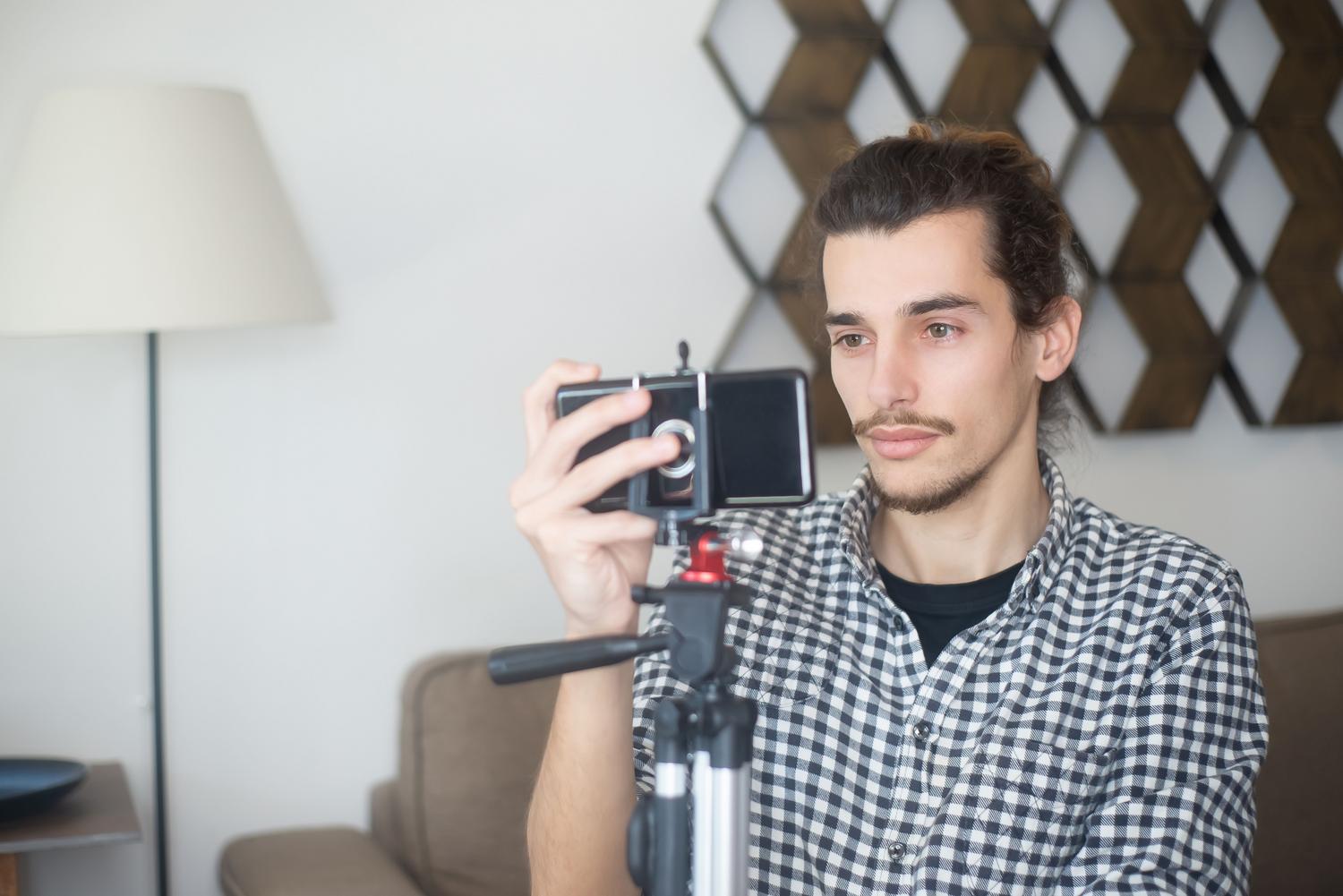 Joven configurando un smartphone en un trípode para asegurar la estabilidad absoluta en sus tomas de vídeo. Joven configurando un smartphone en un trípode para asegurar la estabilidad absoluta en sus tomas de vídeo.