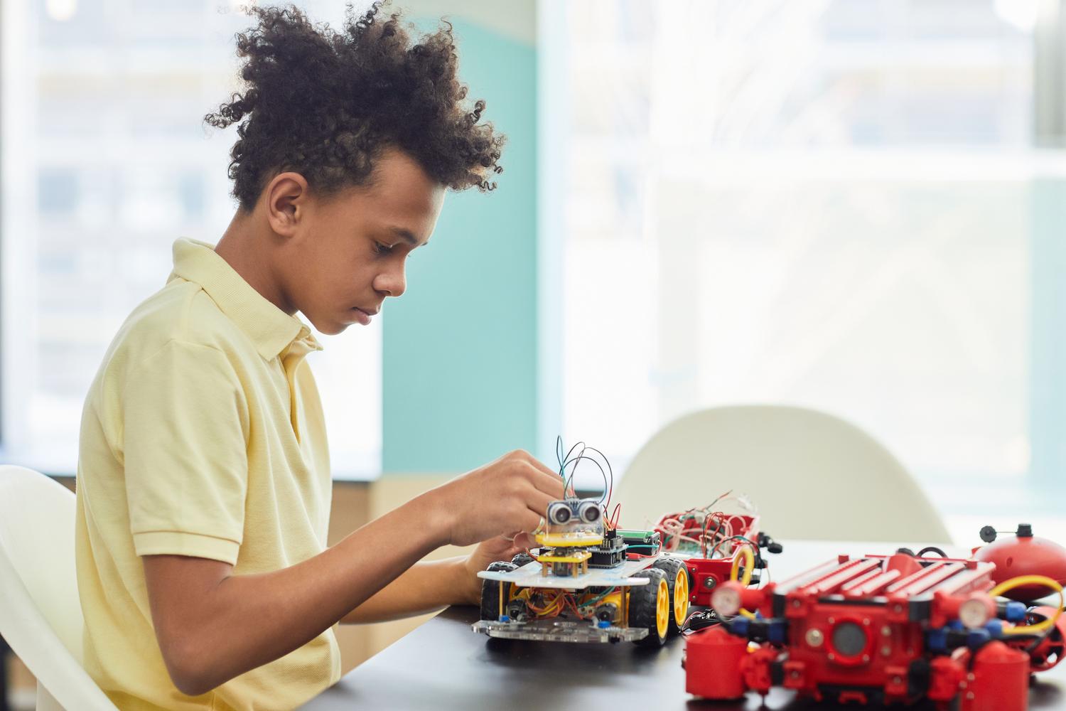 Un estudiante concentrado en el montaje de un pequeño robot con ruedas, fomentando el pensamiento lógico y la ingeniería.