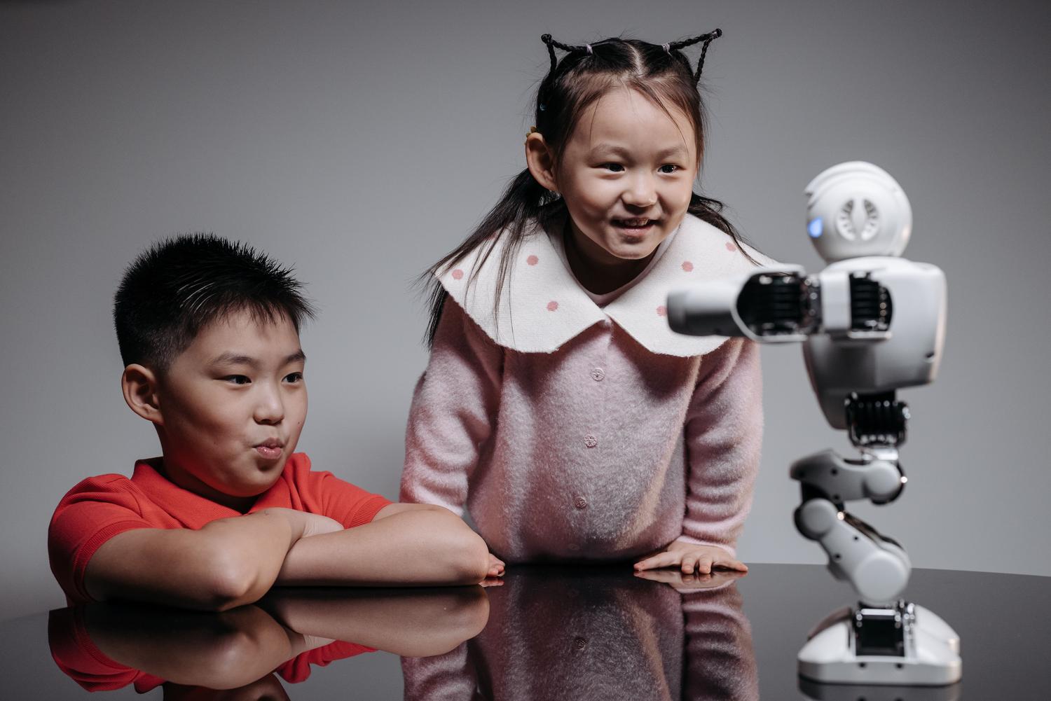 Dos niños interactuando con un pequeño robot humanoide, mostrando la curiosidad y el aprendizaje en la robótica educativa.