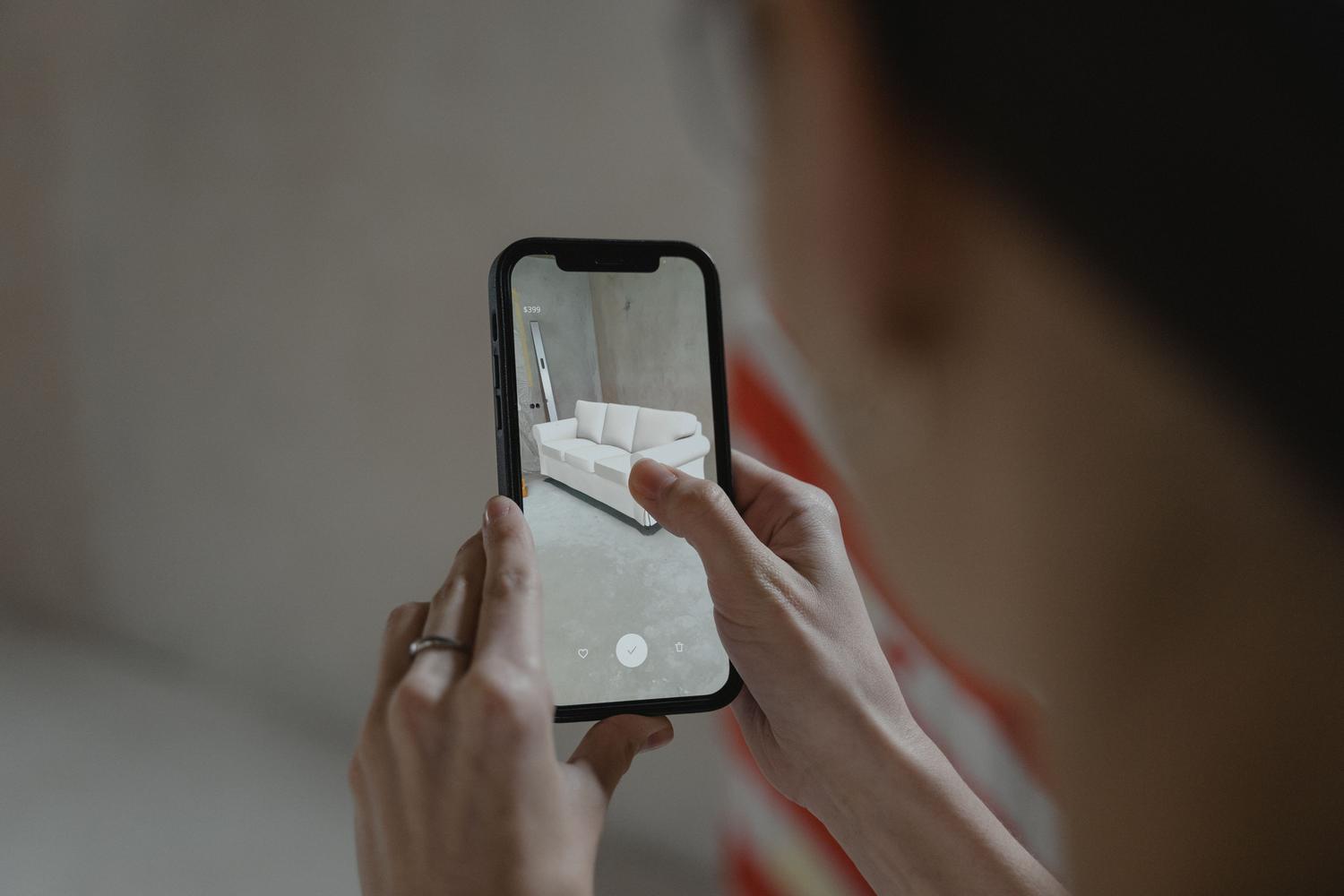 Persona utilizando realidad aumentada en un iPhone para visualizar un sofá en una habitación, ilustrando la planificación de espacios.
