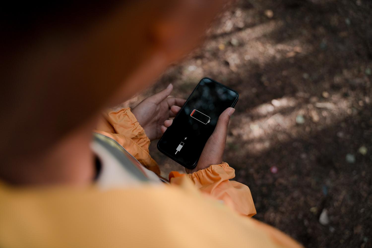 Persona sosteniendo un iPhone con el indicador de batería baja en rojo, ilustrando la frustración de quedarse sin energía.
