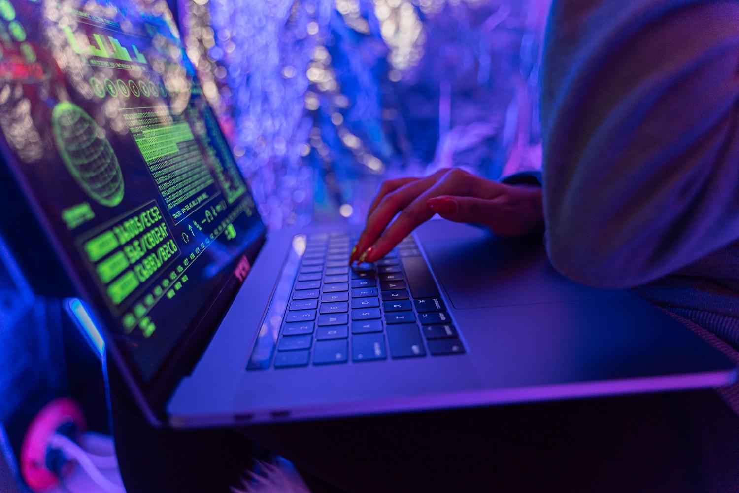 Primer plano de manos escribiendo en un MacBook con gráficos de ciberseguridad en tonos púrpuras, ilustrando que macOS también es vulnerable al phishing.