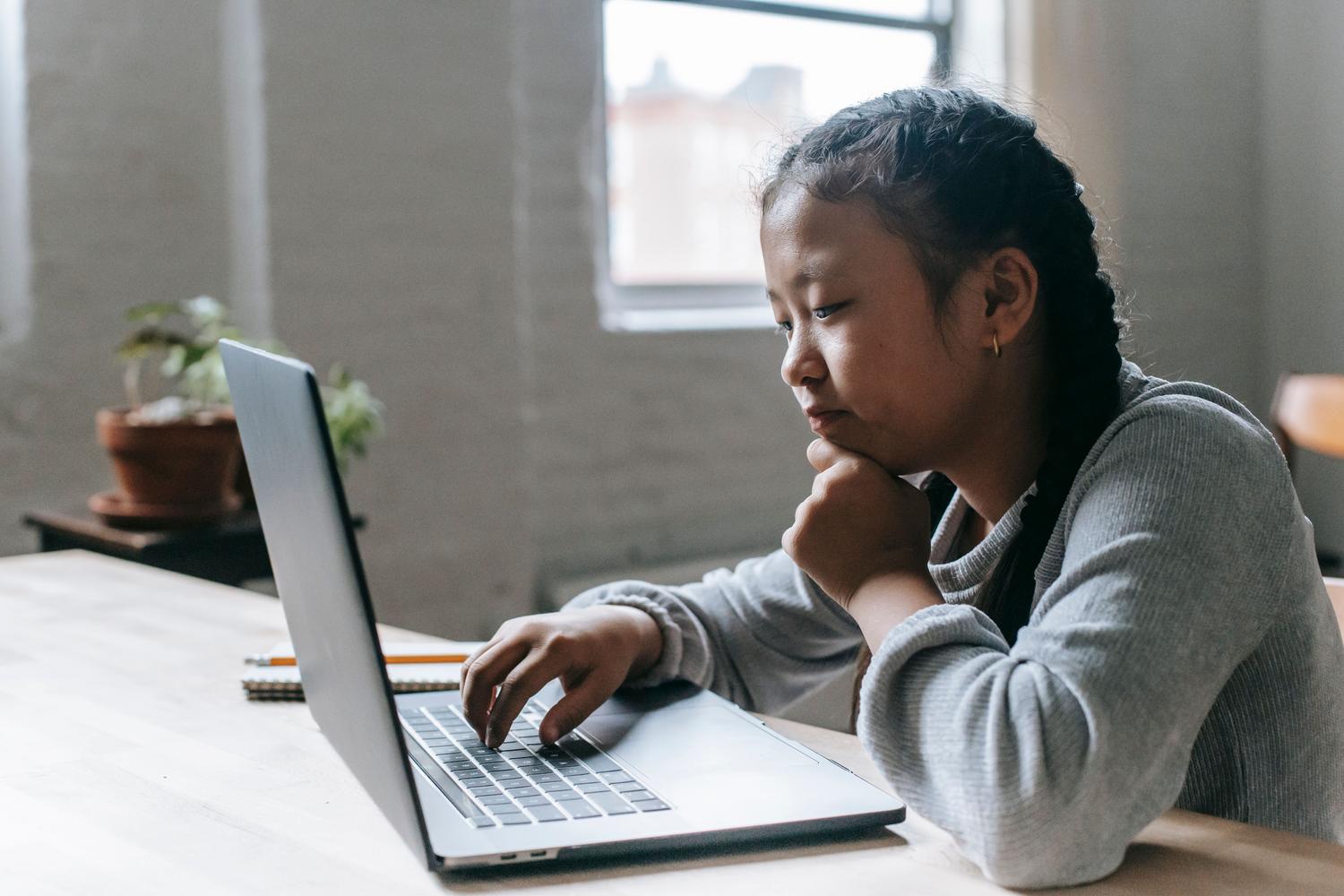 Niña concentrada estudiando con un ordenador portátil, representando la alfabetización mediática y la educación digital.