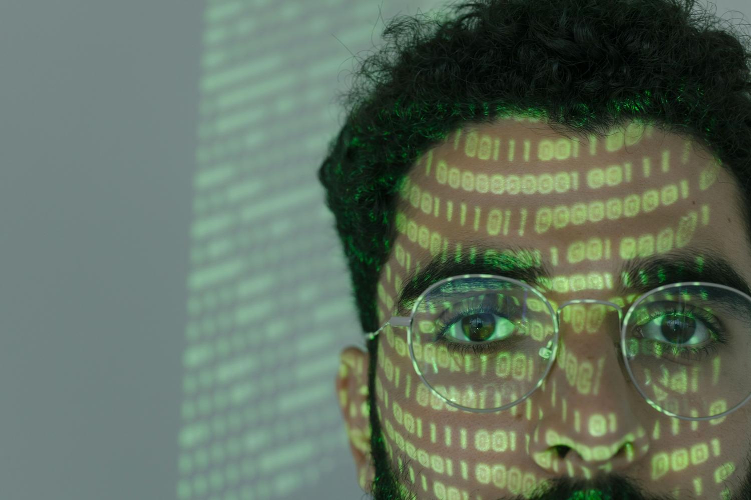 Primer plano de un profesional con código binario proyectado en su rostro, simbolizando el impacto de la inteligencia artificial en la ciberseguridad.