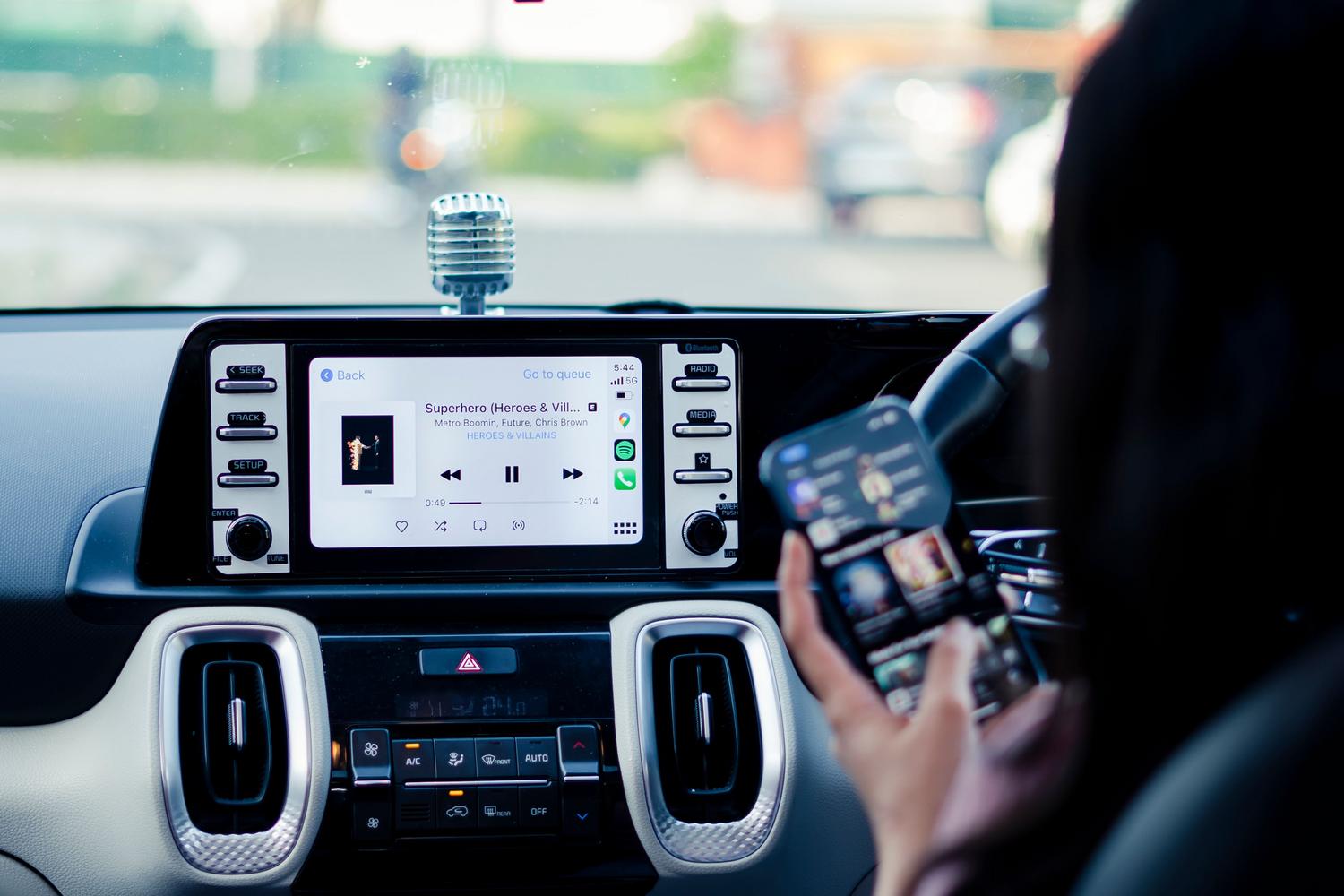 Persona configurando su iPhone mientras se visualiza la interfaz de música de Apple CarPlay en el coche