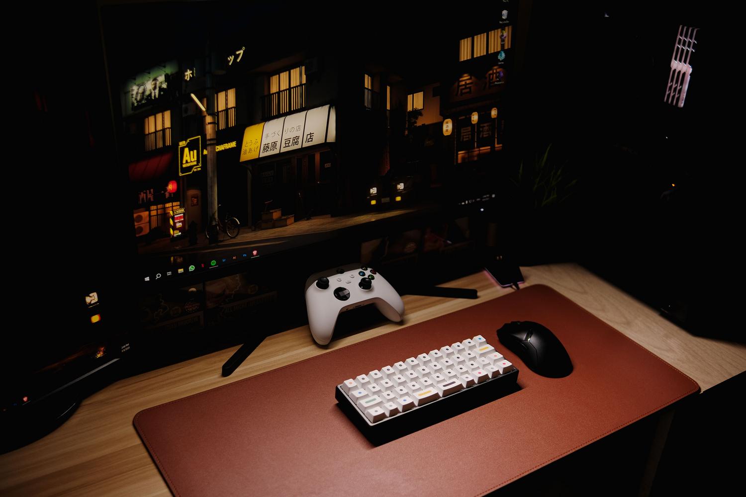 Setup de gaming nocturno con teclado mecánico iluminado, mando de consola y monitor, resaltando el ambiente para jugar.