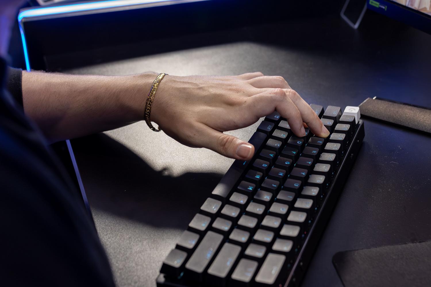 Primer plano de una mano escribiendo en un teclado mecánico con teclas retroiluminadas en un entorno oscuro.