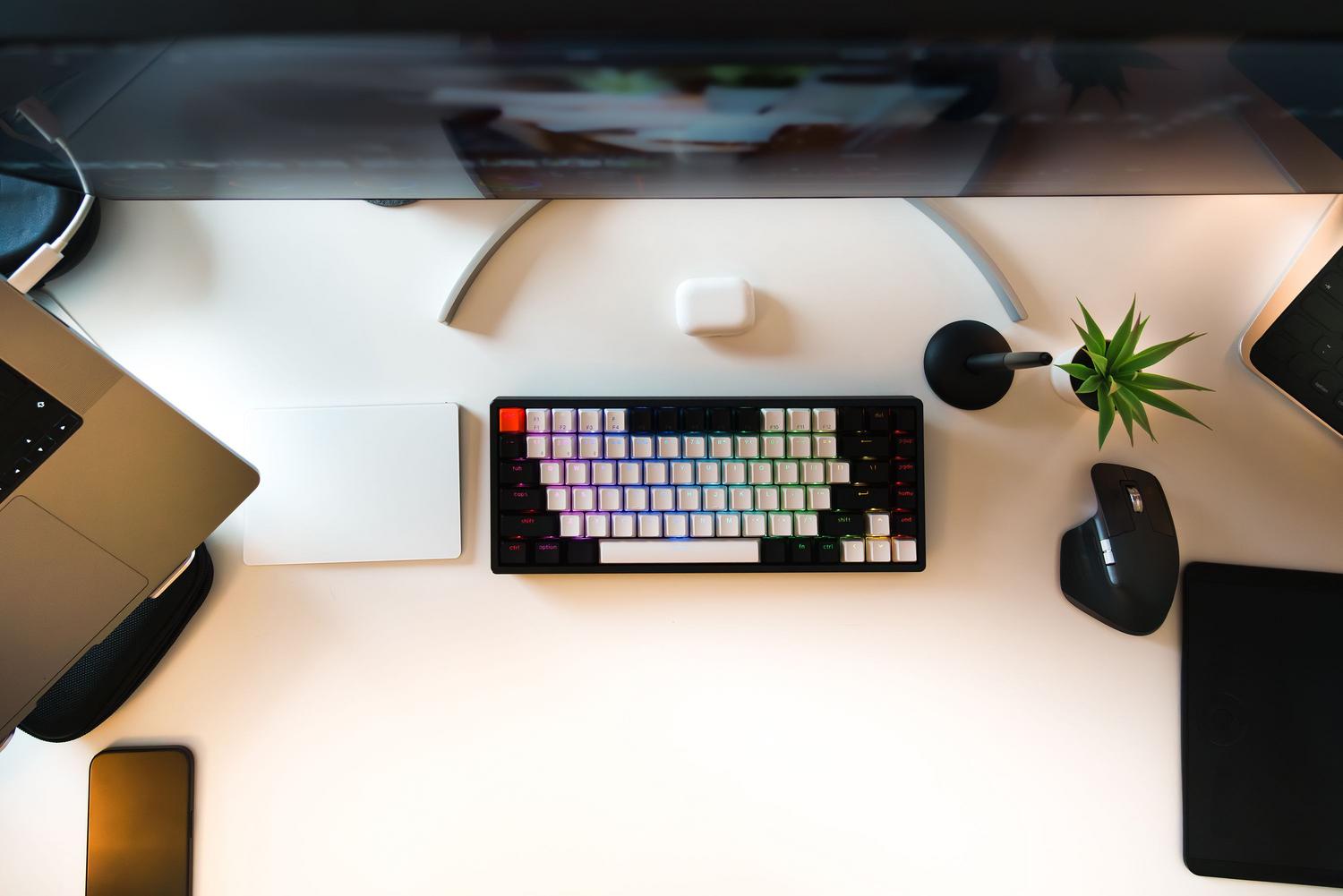 Vista superior de un escritorio de oficina moderno y minimalista con un teclado inalámbrico, gadgets y plantas, ideal para el teletrabajo.