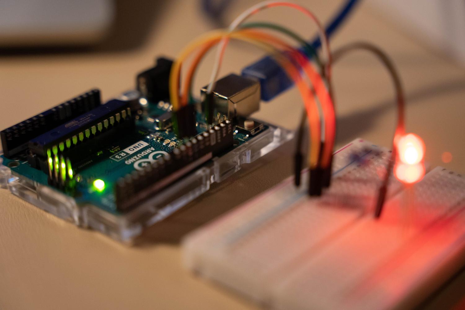 Primer plano de una placa Arduino Uno R3 conectada a una protoboard con cables de colores y LEDs rojos encendidos, representando el prototipado de sistemas embebidos. Primer plano de una placa Arduino Uno R3 conectada a una protoboard con cables de colores y LEDs rojos encendidos, representando el prototipado de sistemas embebidos.