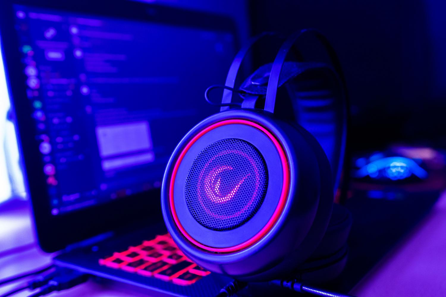 Auriculares gaming con iluminación neón junto a un ordenador, ilustrando la gestión de sonido y música mediante DirectSound y DirectMusic.