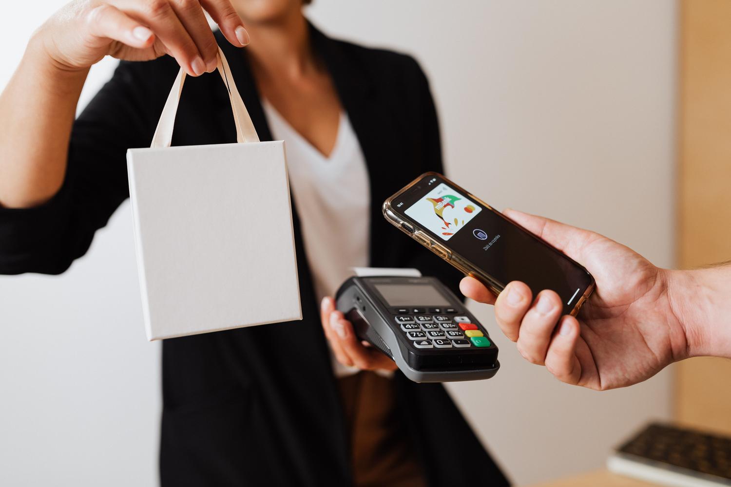 Persona utilizando el móvil para efectuar un pago cashless en un terminal de punto de venta de una tienda