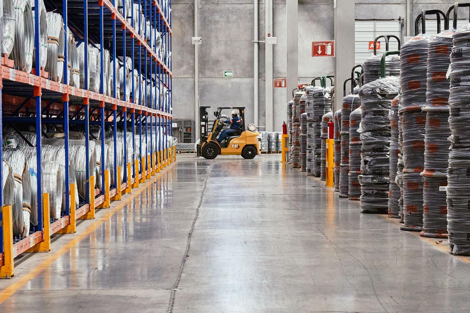 Montacargas operando en un almacén industrial moderno con mercancías organizadas, ilustrando la logística y el almacenamiento físico.