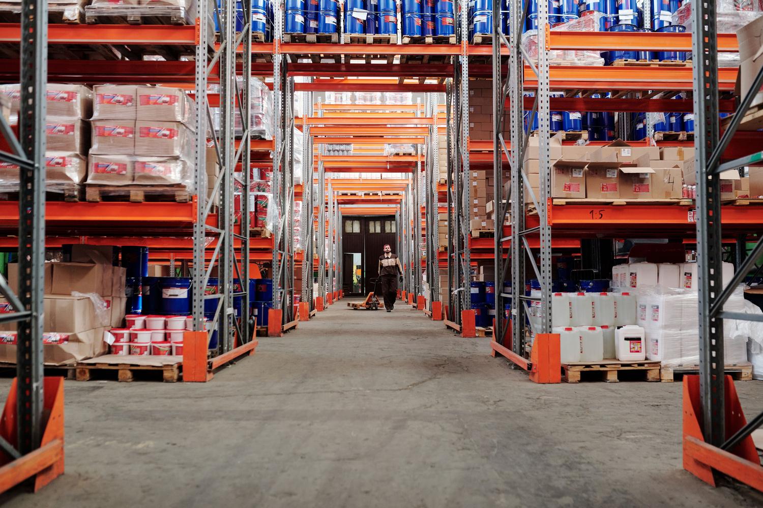 Pasillo amplio de un almacén logístico con estanterías metálicas llenas de stock, mostrando la capacidad de almacenamiento empresarial.