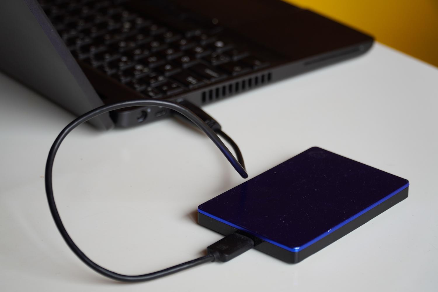 Primer plano de un disco duro externo conectado a un ordenador portátil, representando una de las causas principales que disparan el proceso de indexación mds_stores.