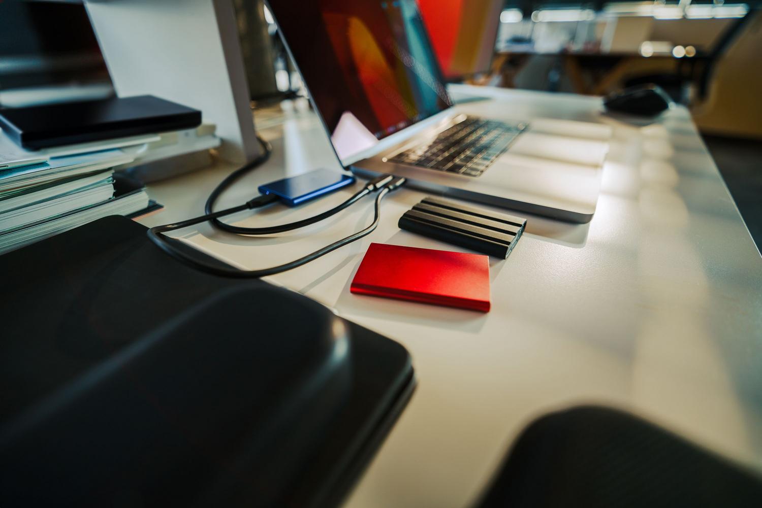 Escritorio de oficina organizado con un ordenador portátil y varios discos duros externos, ilustrando cómo cada unidad conectada genera su propio proceso de indexación.