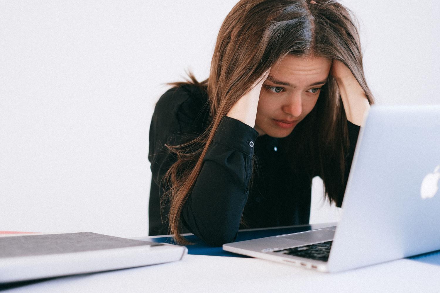 Una mujer con expresión de preocupación y estrés mirando la pantalla de su portátil, ilustrando la frustración cuando el Mac se ralentiza por el alto uso de CPU.