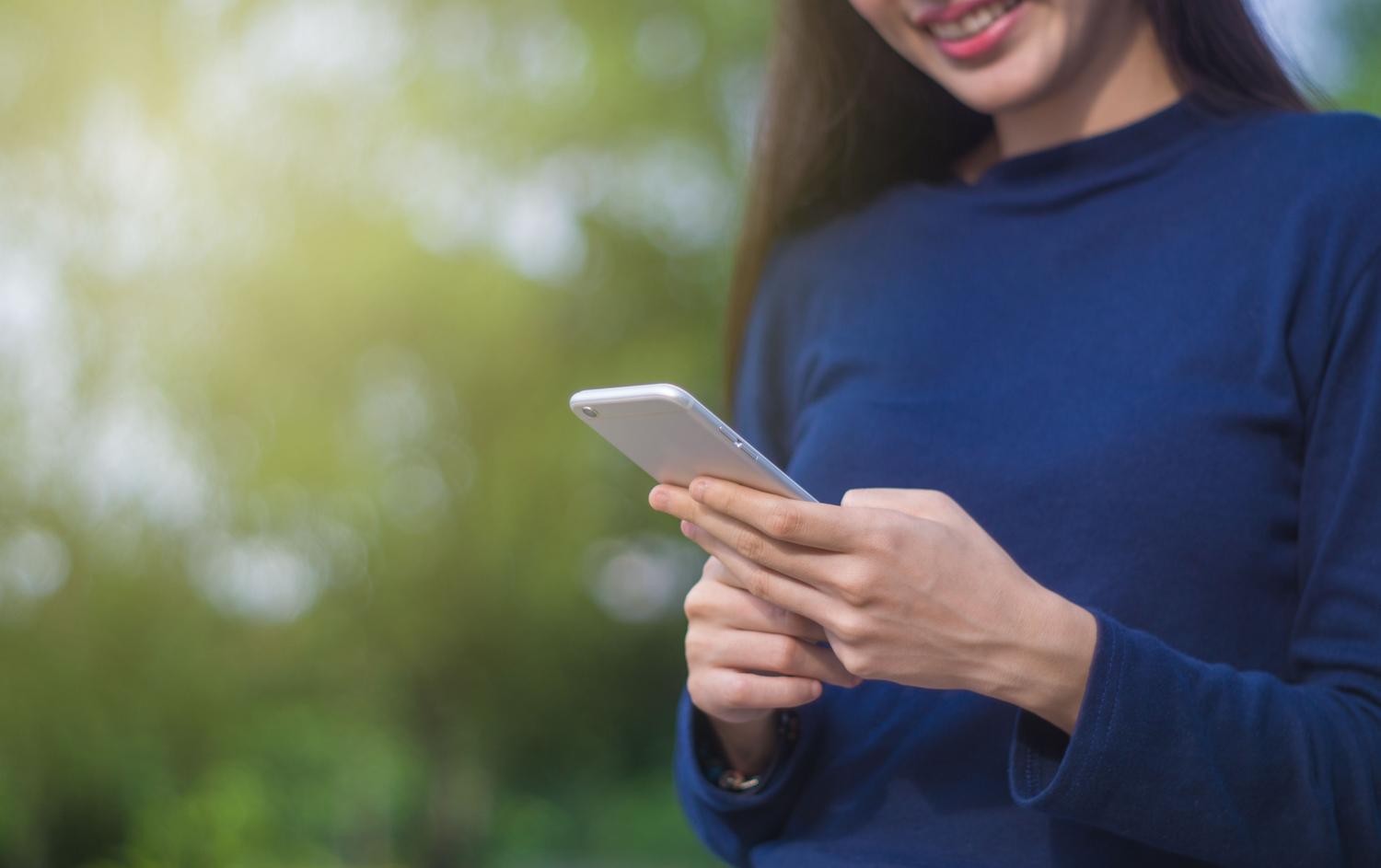 Mujer utilizando un smartphone en un entorno exterior luminoso y natural