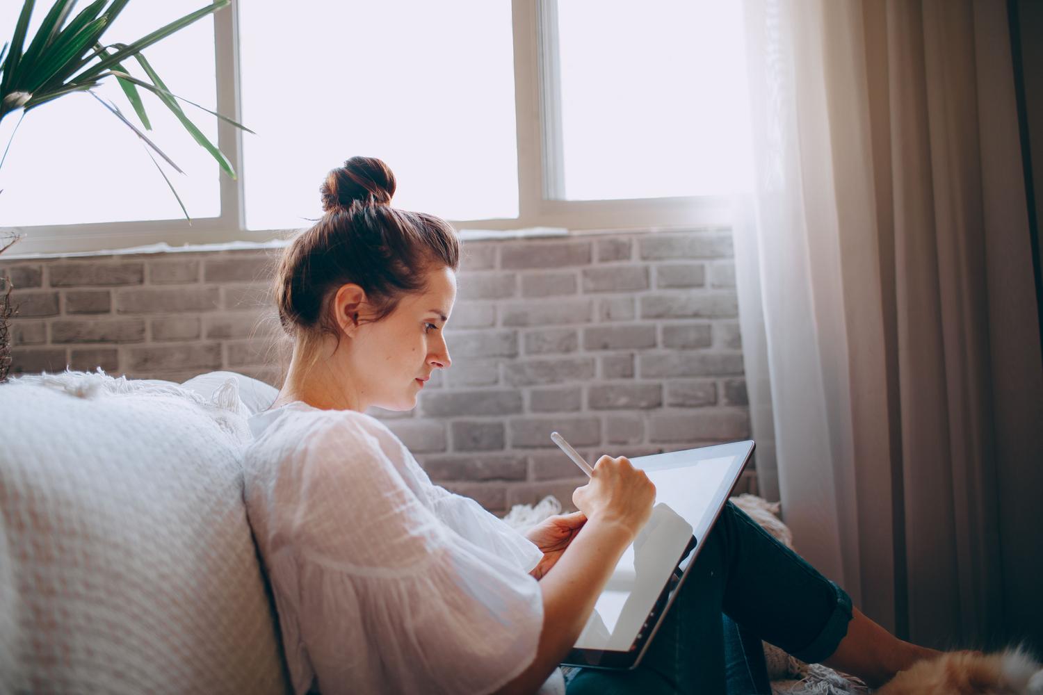 Persona utilizando una tablet de forma relajada en el sofá para tareas cotidianas.