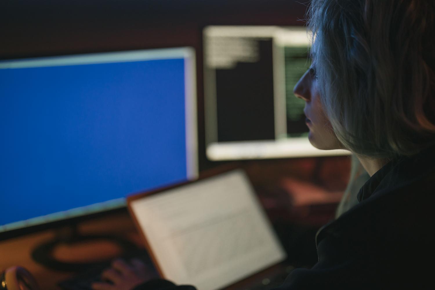 Experta en ciberseguridad analizando datos en múltiples monitores durante la noche, reflejando el enfoque técnico y la gestión de incidentes.