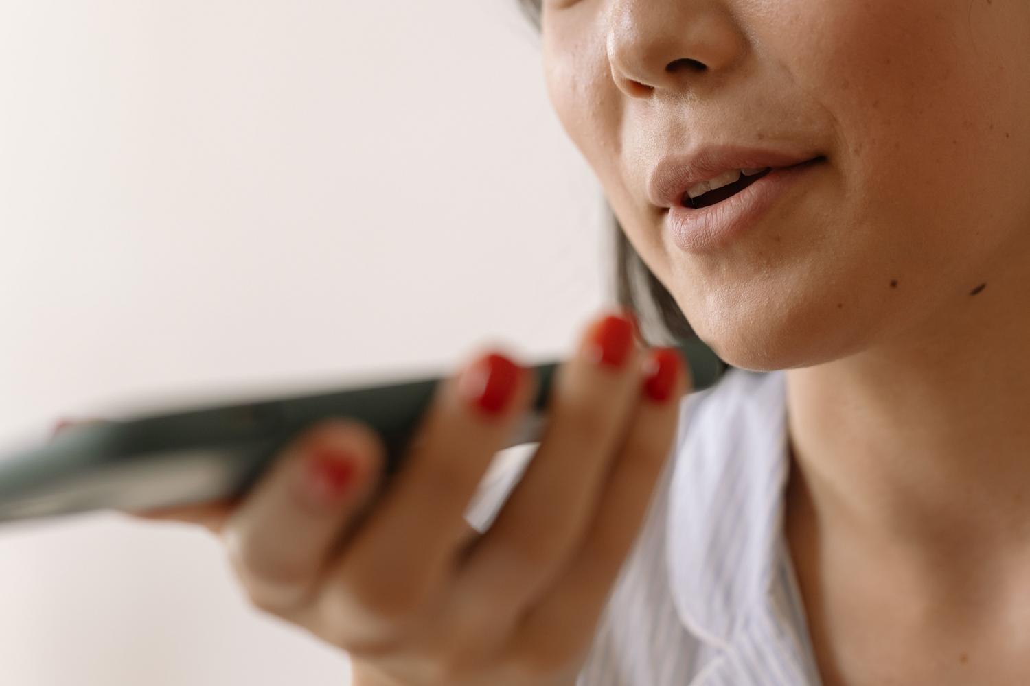Primer plano de una persona hablando al micrófono de un smartphone para grabar una muestra de voz para IA.