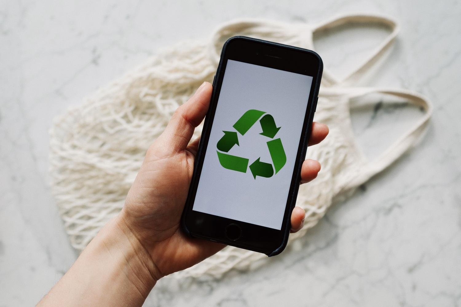 Mano sosteniendo un smartphone con un símbolo de reciclaje, simbolizando la sostenibilidad y el hardware circular.